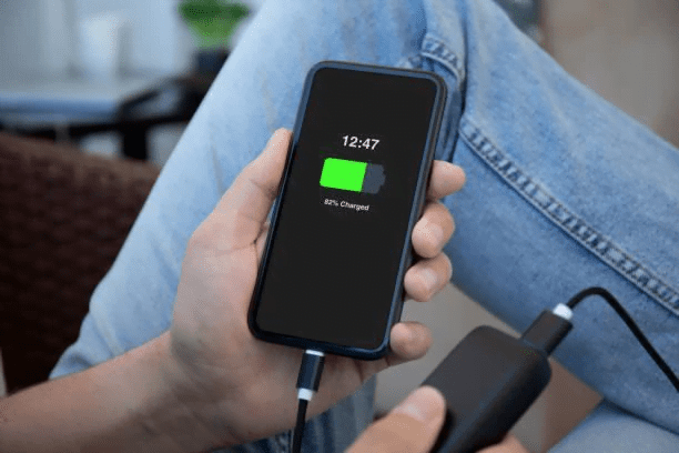 un barbat tine in mana un telefon iphone 13 mini si il incarca cu fir